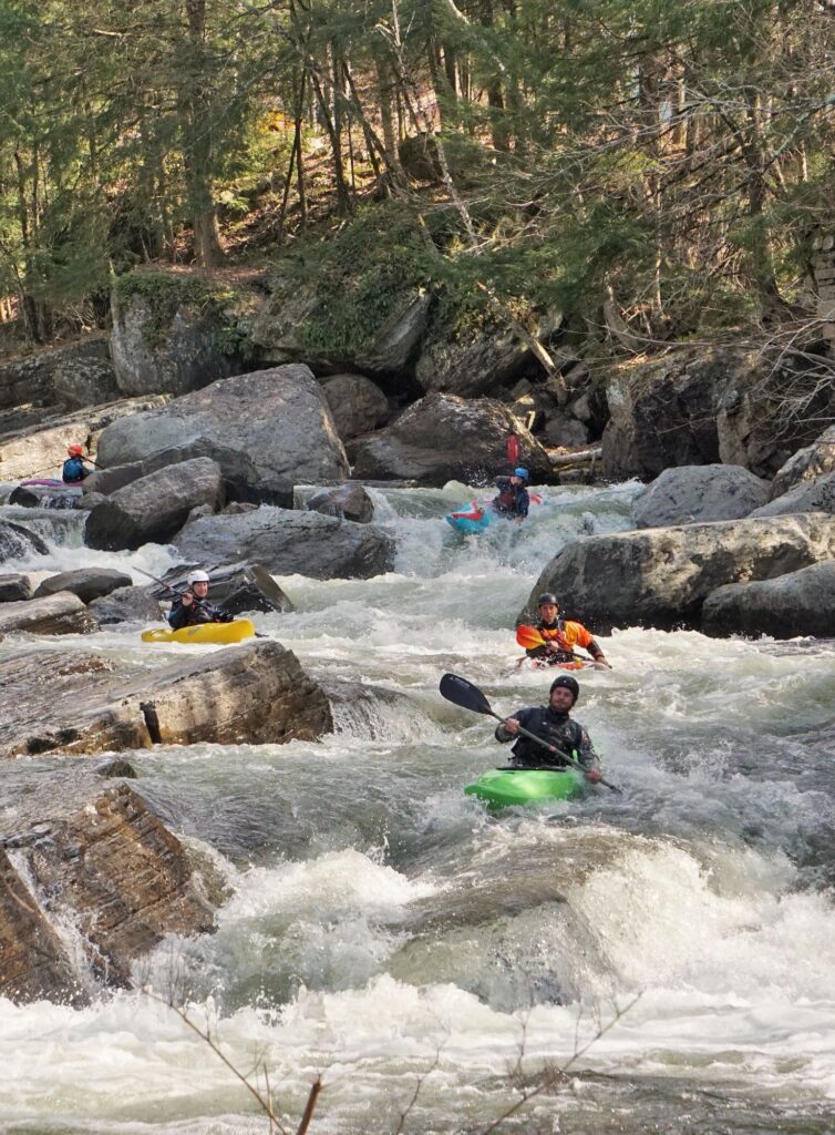 Multiple kayakers coming through the rapids on the New Haven Ledges Vermont whitewater kayaking